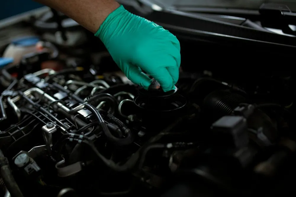 A gloved hand at the oil filler cap of a car engine